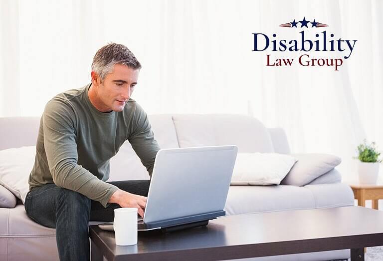 Man typing on computer in living room disability law group logo