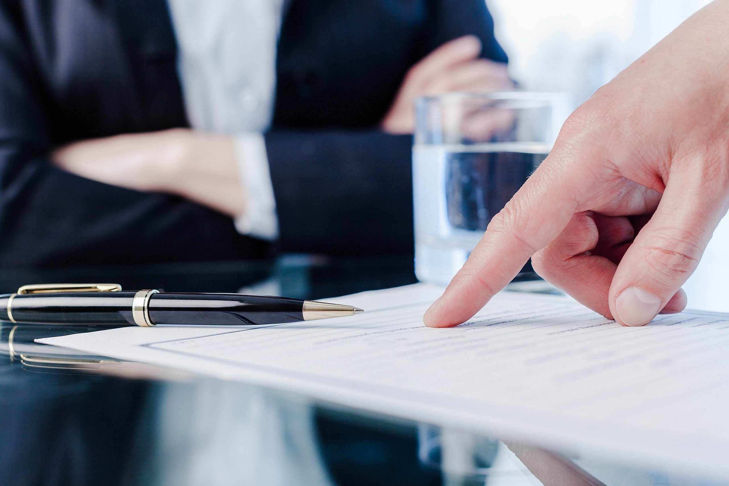 lawyer sitting with arms folded and person pointing at paper