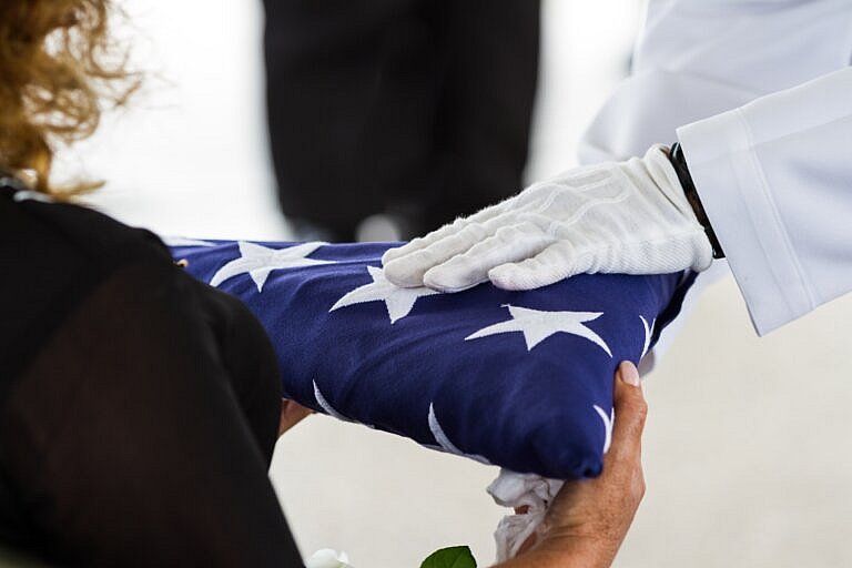 Veterans widow receiving folded American flag at military funeral for survivor benefits claim assistance