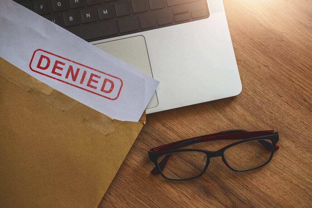 Document with denied stamp on the laptop on wooden table.