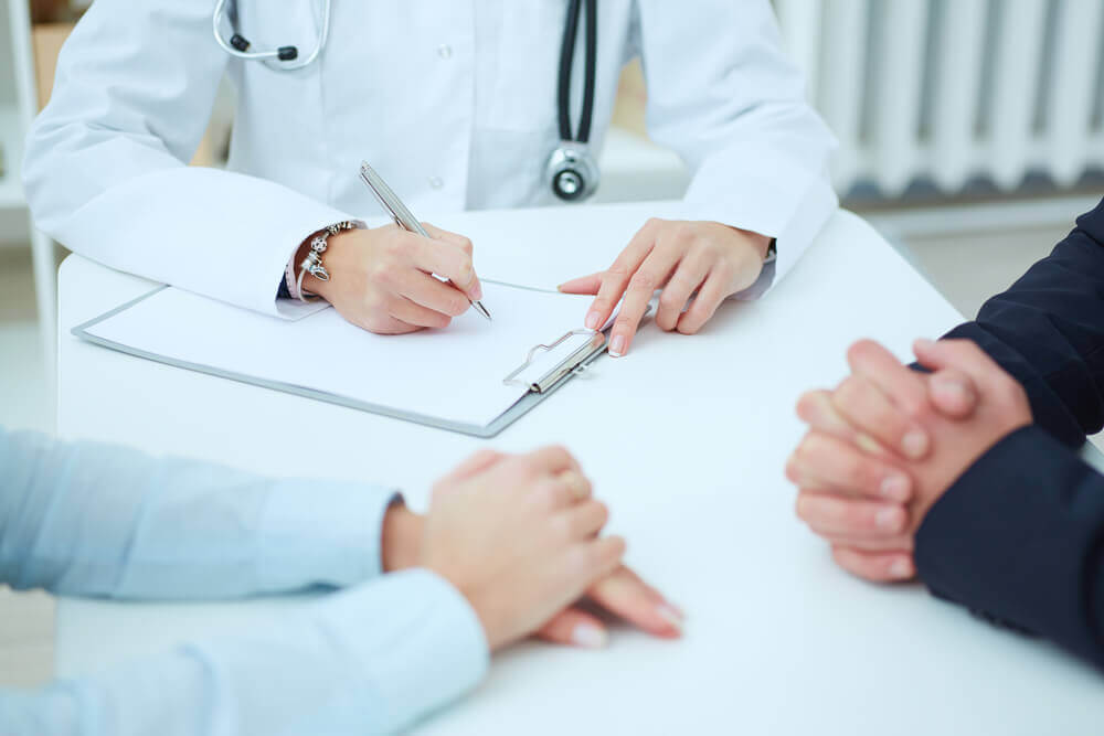 Closeup of patients hands and doctor taking notes.