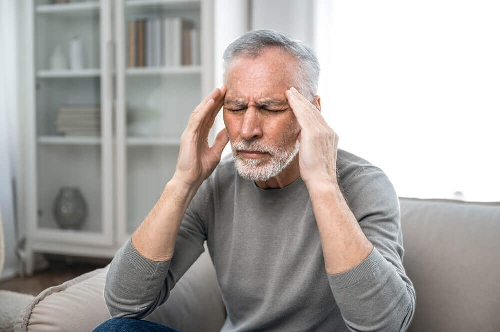 Portrait of tired unhealthy senior man massaging temples, suffering from terrible headache or migraine.