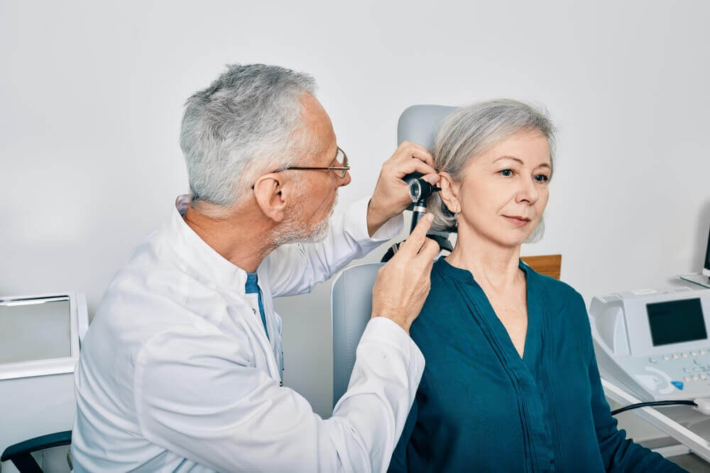 Otolaryngologist doctor checking senior woman's ear using otoscope or auriscope at hearing center.