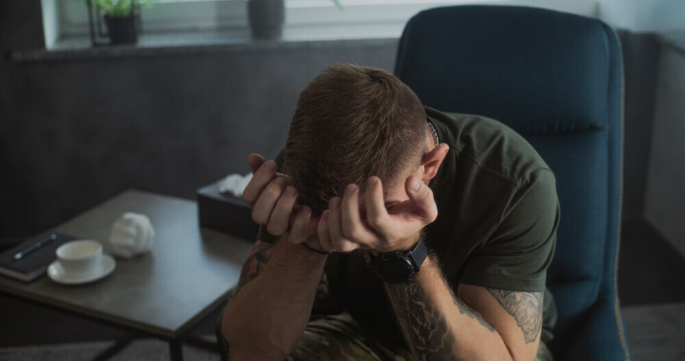 Veteran struggling with PTSD during therapy session, seeking VA disability benefits and mental health support