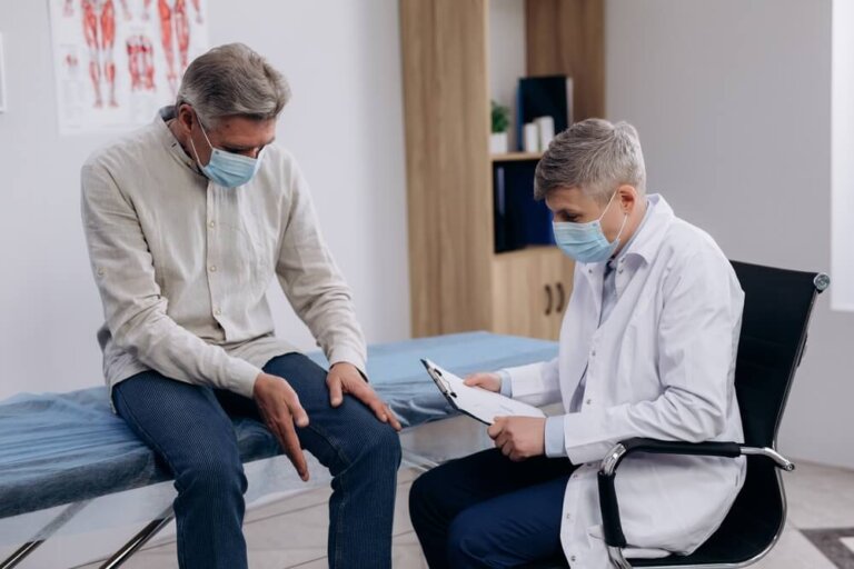 Elderly patient wearing medical mask talking to male family therapist during regular doctors appointment.
