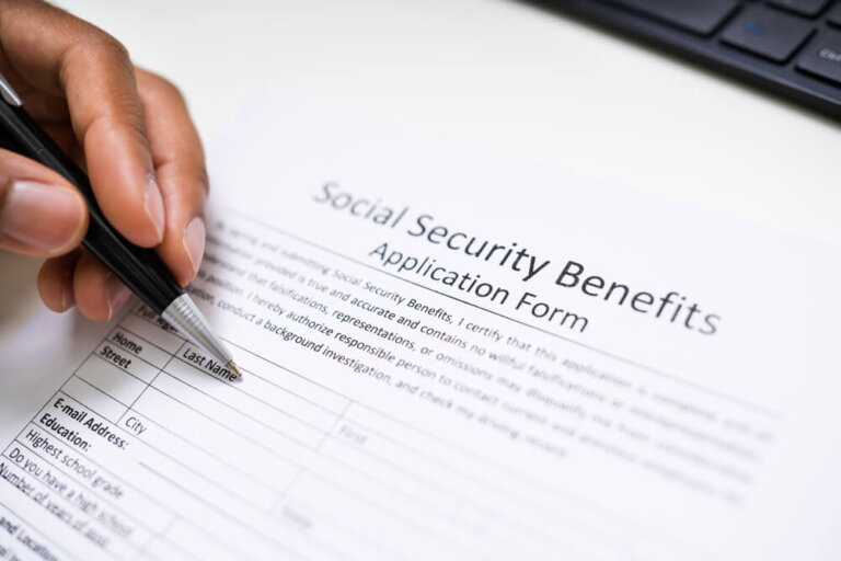 Close-up Of A Person's Hand Filling Social Security Benefits Application Form