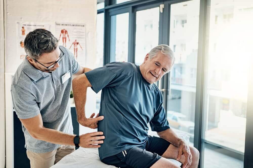 Physio therapist, chiropractor and senior man with back pain for rehabilitation, consulting and exercise.