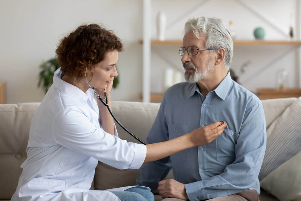 Doctor checking heartbeat examining elder retired man at home. Seniors heart diseases, cardiology concept.