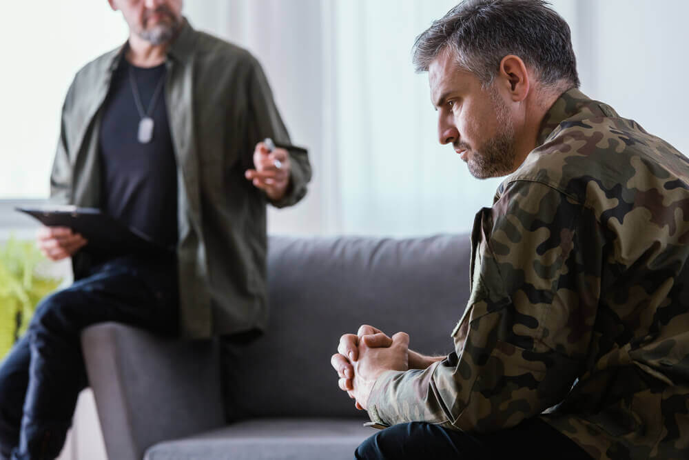 Veteran in camouflage uniform discussing mental health with counselor during VA disability claim evaluation