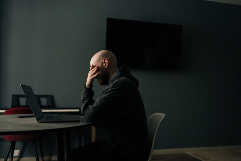 Stressed bald man overing face with hand while sitting at desk in home office, feeling tired and overwhelmed by the social security disability application process.