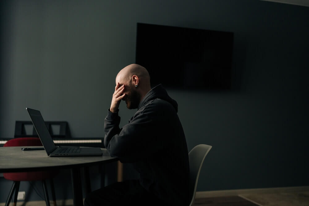 Stressed bald man overing face with hand while sitting at desk in home office, feeling tired and overwhelmed by the social security disability application process.
