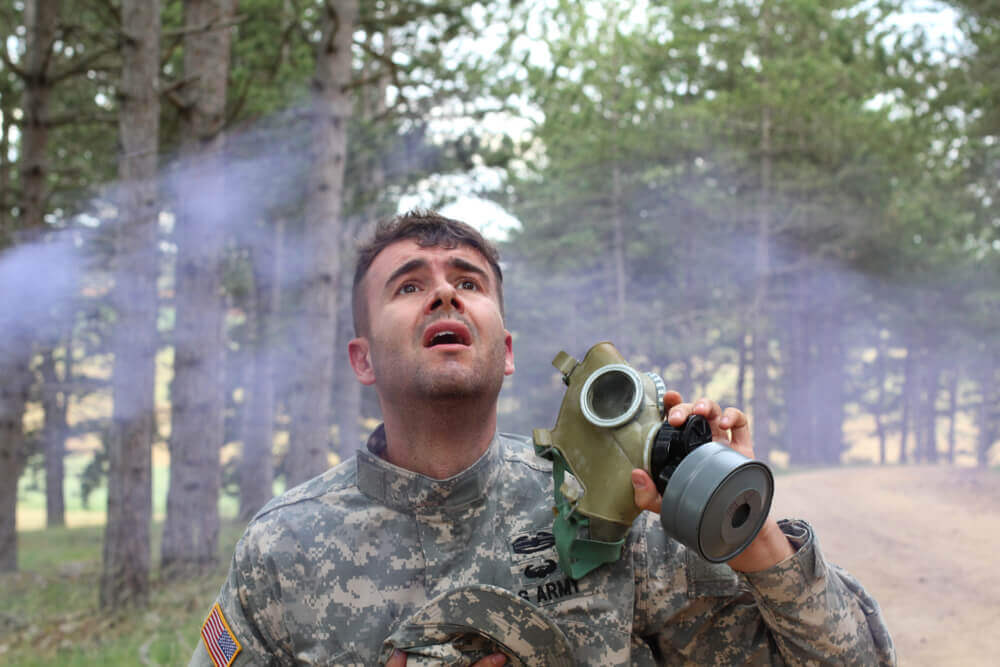 U.S. Army veteran exposed to toxic fumes holding a gas mask, illustrating toxic exposure claims for VA benefits in Michigan.